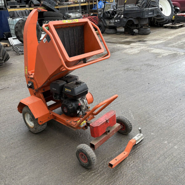 Orange portable industrial machine with a gas engine in a yard full of tires and machinery on a concrete surface, outdoors