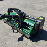 Industrial green wood chipper attachment with black hydraulic arm, mounted on a concrete surface.