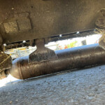 Close-up view of a muddy metal linkage under a vehicle, with grass clippings attached to it.