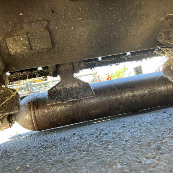 Close-up view of a muddy metal linkage under a vehicle, with grass clippings attached to it.