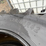 Close-up of a tire with severe tread damage and jagged missing sections, with a white IBC container and fence in the background.
