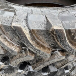 Pile of jagged broken glass shards scattered on muddy ground, with grime and dirt coating them
