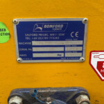 Blue Bomford Turner identification plate on a yellow machine, with a green 'PASSED INSPECTION' sticker to the left.