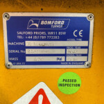 Close-up of a blue Bomford Turner machine nameplate on a yellow surface, showing model and serial information and a CE mark.