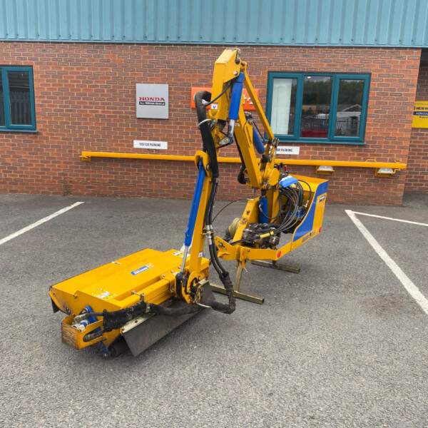 Yellow hydraulic construction machine with exposed hoses parked in a lot in front of a brick building with a blue door and Honda sign behind it.