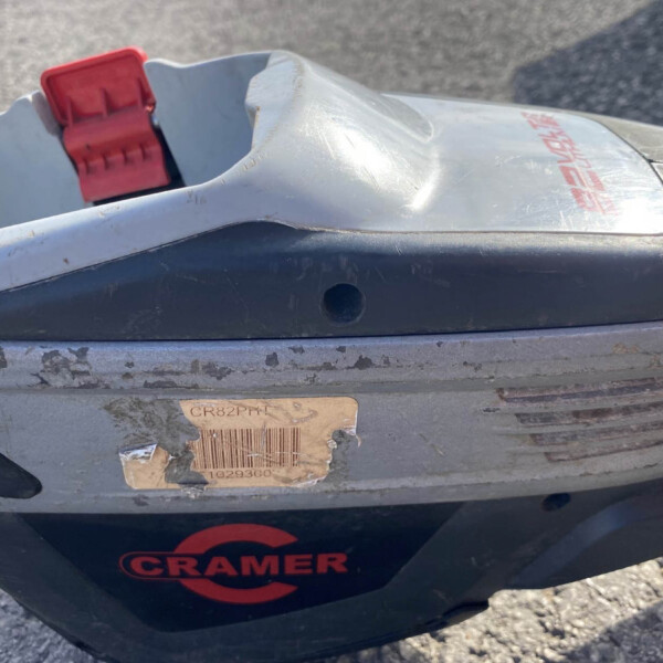 Close-up of a dirty gray plastic device with a red latch and a worn CRAMER sticker; appears to be a power tool accessory or component.