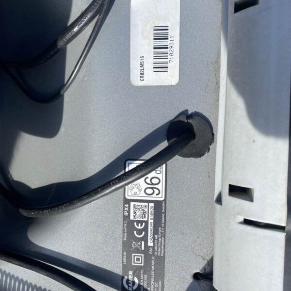Close-up of a white barcode label on a gray metal panel with black cables nearby.
