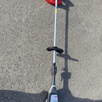 Top-down view of a cordless string trimmer with a red guard resting on rough asphalt driveway surface