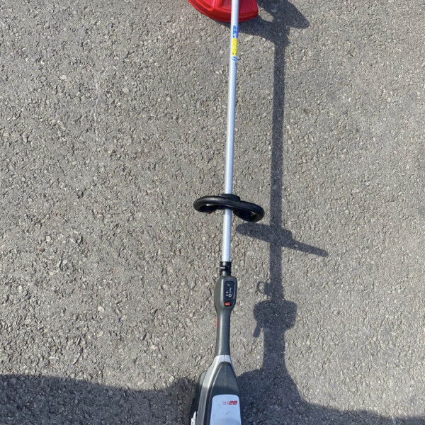 Top-down view of a cordless string trimmer with a red guard resting on rough asphalt driveway surface