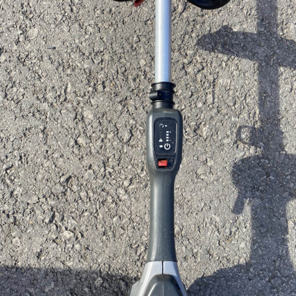 Metal detector with control panel and long shaft resting on rough asphalt surface, seen from above.
