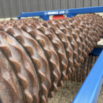 Rusty corrugated metal sheets coiled on a blue Minimax 630 roller frame outdoors in a yard.