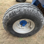 Close-up of a large off-road tractor tire with a blue wheel hub on a dry grassy field.