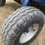 Close-up of a large, rugged tire on a blue off-road vehicle, dusty ground beneath.