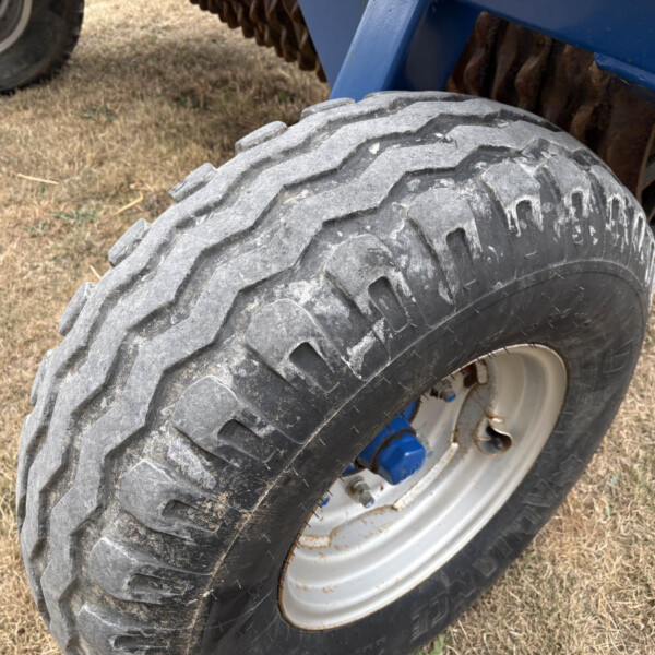 Close-up of a large, rugged tire on a blue off-road vehicle, dusty ground beneath.