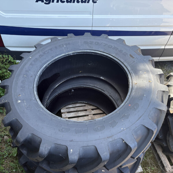Stack of large tractor tires leaning against a white van in a garden setting with greenery and flowers nearby.