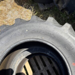 Close-up of a large off-road tire with jagged tread resting on wooden pallets outdoors.
