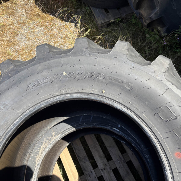 Close-up of a large off-road tire with jagged tread resting on wooden pallets outdoors.
