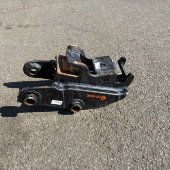 Rusted metal heavy equipment attachment resting on an asphalt surface, painted black and orange with wheels and mounting holes visible