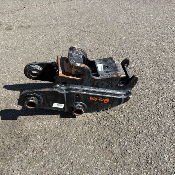 Rusted metal heavy equipment attachment resting on an asphalt surface, painted black and orange with wheels and mounting holes visible
