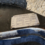 Close-up of a rusted metal plate with an informational label from Harford Attachments Ltd, showing model/serial fields.