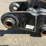 Close-up of a rusted industrial hinge/connector with welded seams and circular openings on heavy equipment.