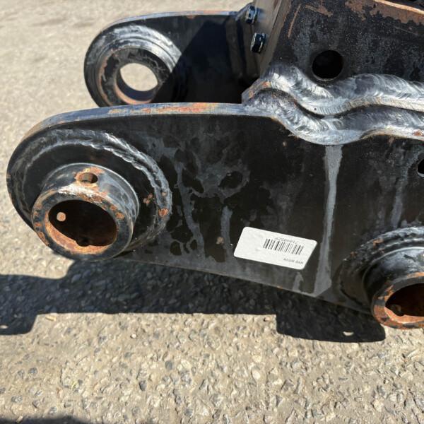 Close-up of a rusted industrial hinge/connector with welded seams and circular openings on heavy equipment.