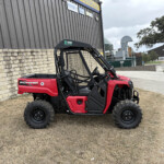 Red Polaris Pioneer 520 side-by-side UTV parked on dry grass beside a stone wall and an industrial metal building with signs above.
