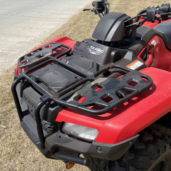 Red ATV with black front cargo rack, handlebars, and headlight visible on a dry grassy area.