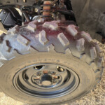 Close-up of a large knobby off-road tire with the wheel and rusty suspension components visible in the wheel well.
