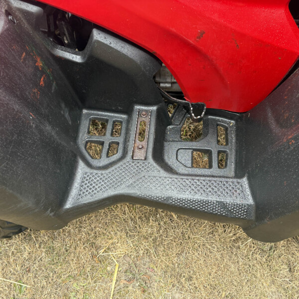 Close-up of a red motorcycle fairing over a black plastic frame, with a metal latch and dirt, on brown grass ground.