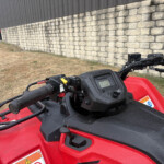 Close-up of the ATV handlebar and instrument panel with a stone wall in the background.