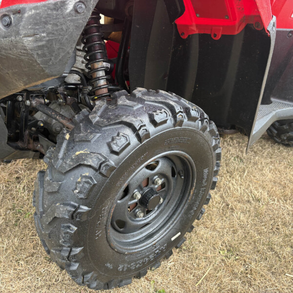 Close-up of an off-road vehicle's front wheel and suspension with dirt and an orange side marker light nearby.