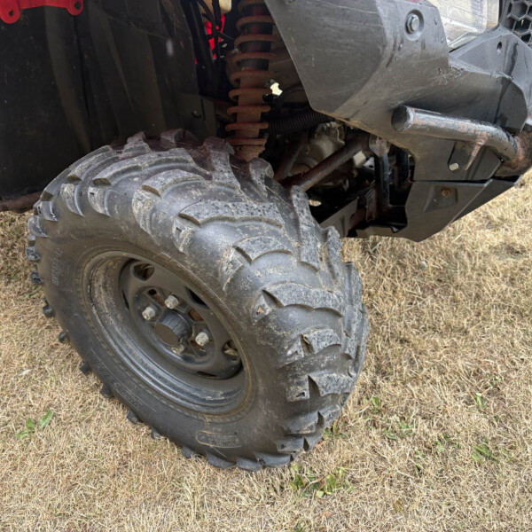 Close-up of a muddy off-road vehicle wheel and suspension showing large tread tire and rusted components.