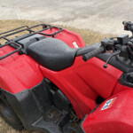 Red ATV with a black front cargo rack and wet seat, viewed from above.