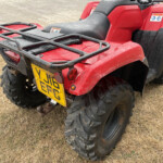 Rear view of a red ATV with a metal cargo rack, dirt splatters, and a yellow UK license plate at the back.