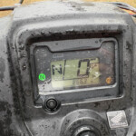 Mud-splattered Honda ATV dashboard with a green 'N' gear indicator and a numeric display visible behind the glass.