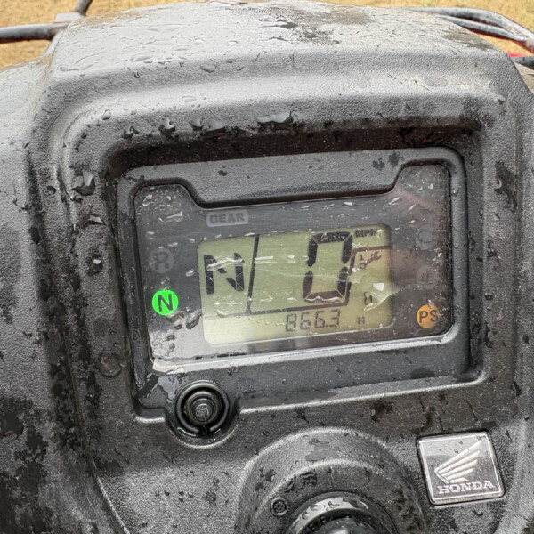Mud-splattered Honda ATV dashboard with a green 'N' gear indicator and a numeric display visible behind the glass.