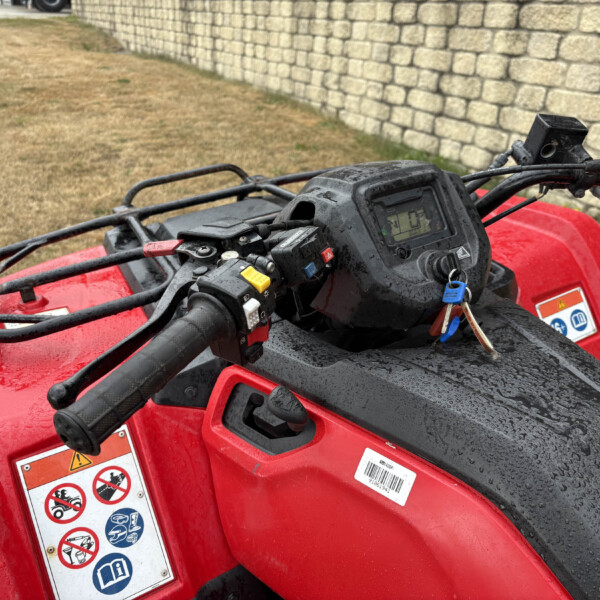 Close-up of a red ATV handlebar and dashboard with wet surfaces, keys in the ignition.