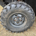 Close-up of a muddy, heavy-duty off-road tire and rim on a vehicle with deep tread patterns.",