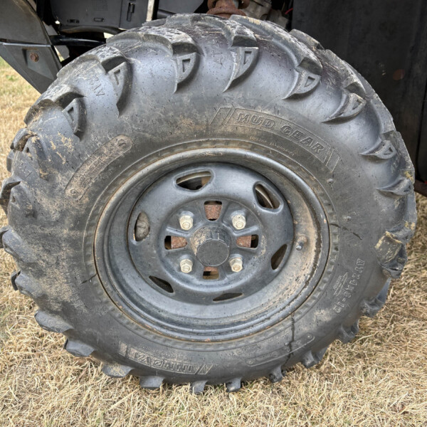 Close-up of a muddy, heavy-duty off-road tire and rim on a vehicle with deep tread patterns.",