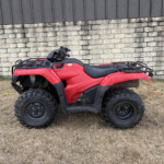 Red ATV parked on dry grass with a stone wall and gray wooden fence in the background.