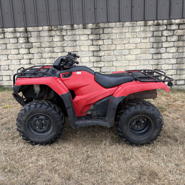 Red ATV parked on dry grass with a stone wall and gray wooden fence in the background.