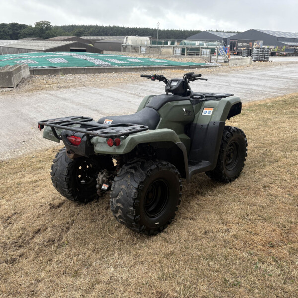 Green ATV parked on dry grass in an industrial yard with warehouses in the background