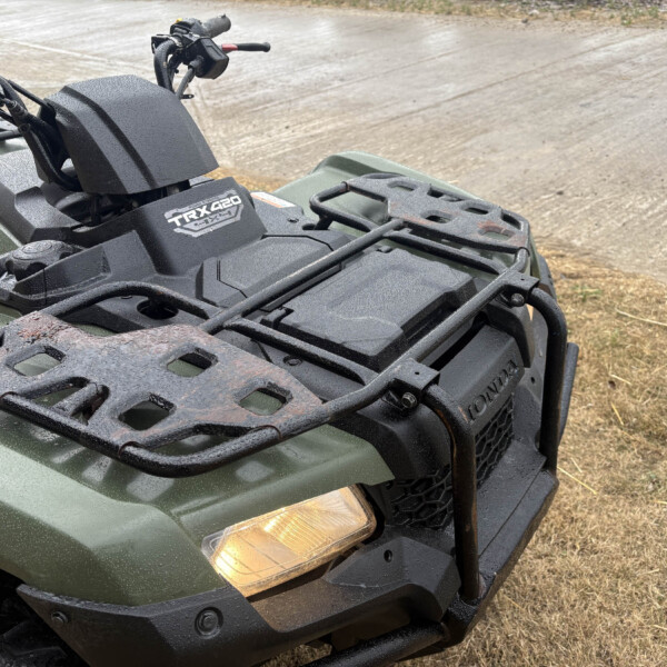 Close-up of an ATV front end showing a green body, black plastic rack, and frosty windshield with the TRX420 badge visible on the hood edge.