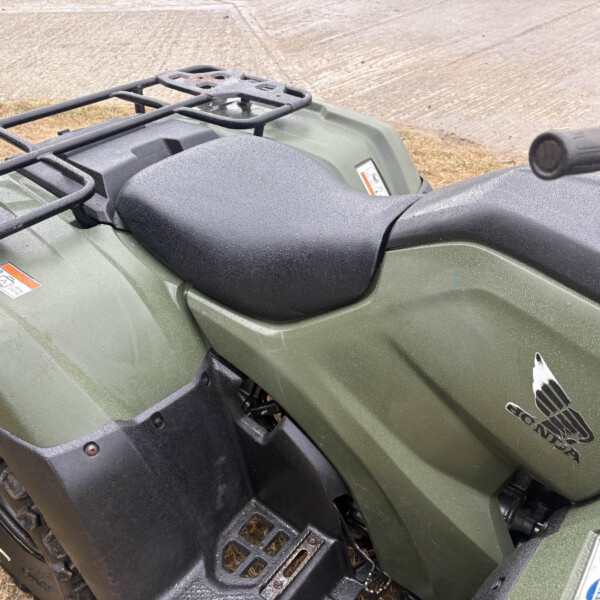 Front view of a green ATV showing a metal cargo rack, rugged seat, and handlebars outdoors on dirt.