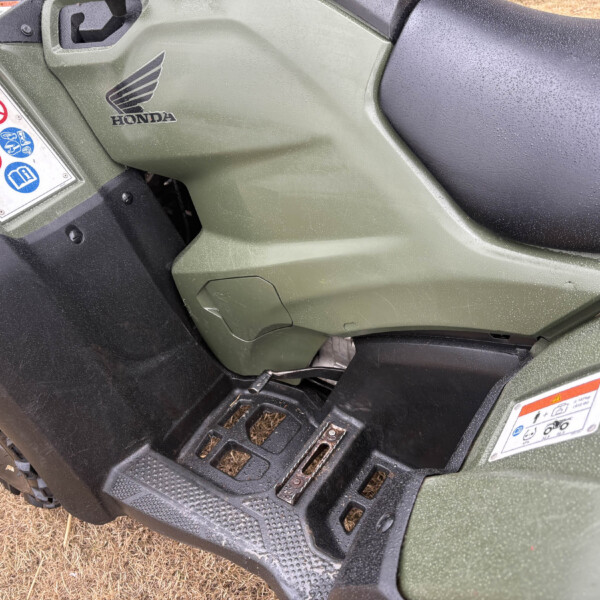 Close-up of a green Honda ATV body with a black seat and textured footboard, rain droplets visible on the surface.