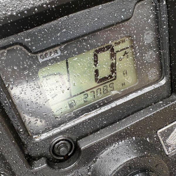 Close-up of a digital display on a rugged control panel, the surface covered in raindrops with a small numeric readout and icons visible behind the glass.