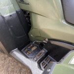 Close-up of a green Honda vehicle panel with a black textured step and a partially visible warning label, surface dusty.