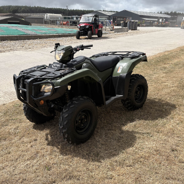Green all-terrain vehicle parked on a dusty construction site with heavy equipment in the background.