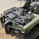 Front view of olive green ATV with a black cargo rack, headlight, and TRX520 badge.